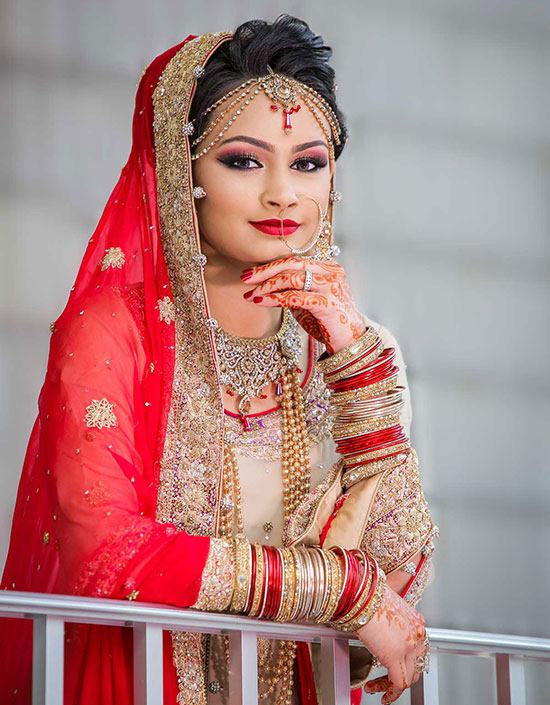 Elegant Indian bride in a traditional red lehenga, adorned with intricate gold jewelry and henna, exudes grace and culture.